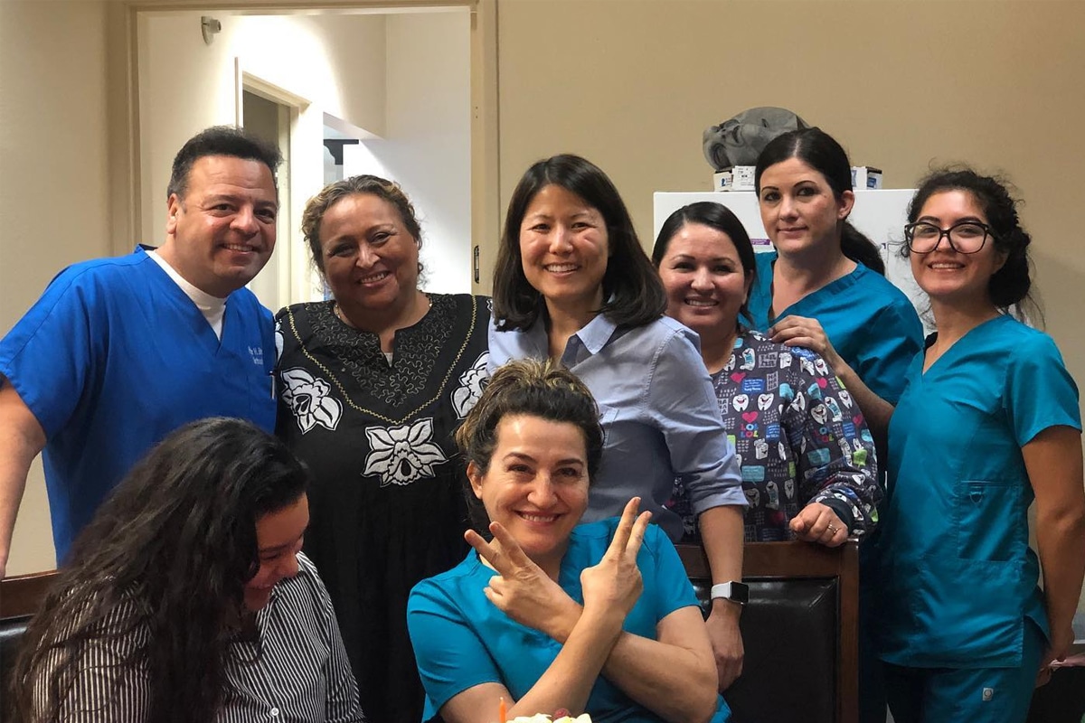 Orthodontics team members wearing blue scrubs smiling together in a clinical office setting.