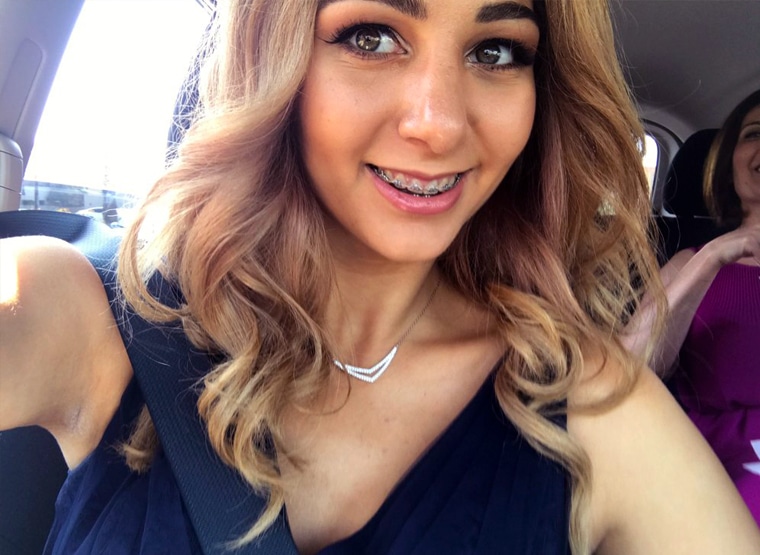 Woman smiling at camera in car wearing dark top and silver necklace
