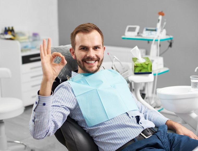 Happy male patient in dental chair giving thumbs up in orthodontist office