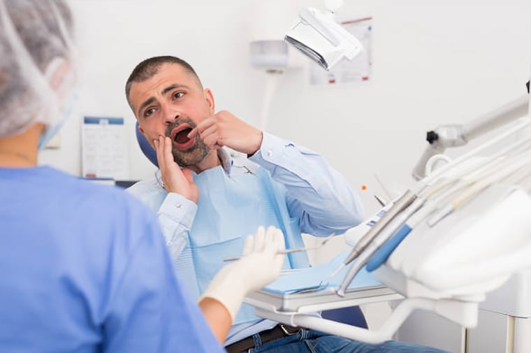 Patient in dental chair experiencing tooth pain during orthodontic examination with dentist.