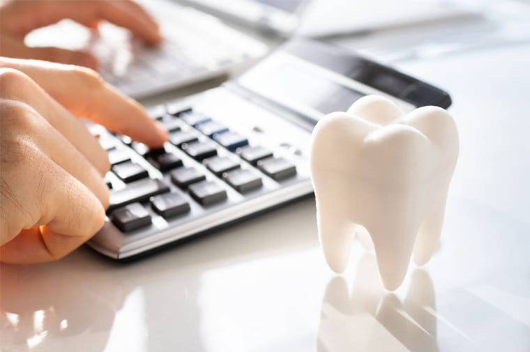 Person using calculator at desk with tooth model, dental office setting