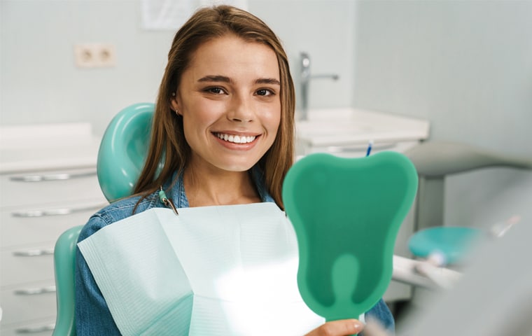 Smiling young woman in dental chair holding green orthodontic model in modern dental office.