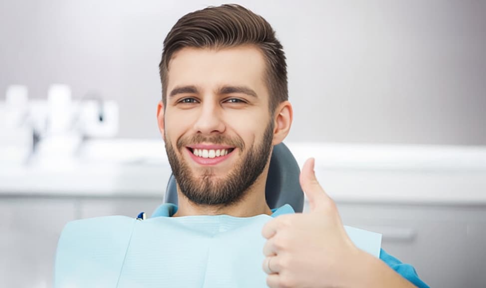 Smiling man giving thumbs up in dental office wearing blue bib
