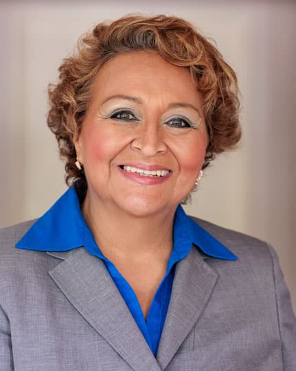Professional headshot of a smiling woman in business attire against neutral background.
