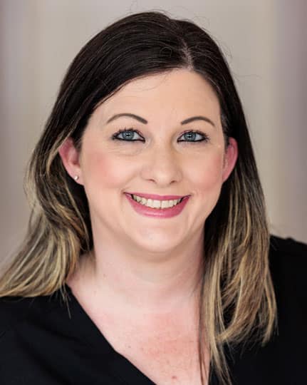 Professional headshot of smiling woman with dark hair against neutral gray background for orthodontics practice.