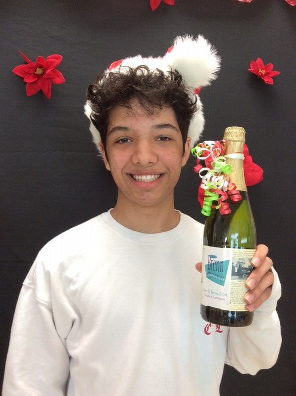 Young person holding decorated holiday bottle against festive red and white backdrop.