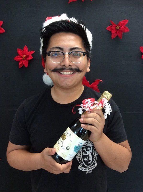 Young man wearing glasses and black shirt holding orthodontic product against festive red snowflake backdrop.
