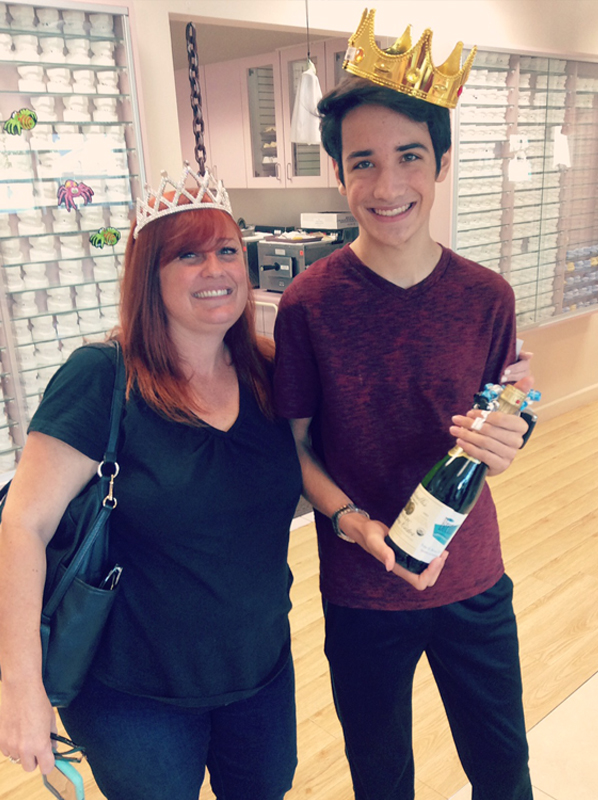 Two people wearing crowns smile together in an orthodontic office holding a beverage.