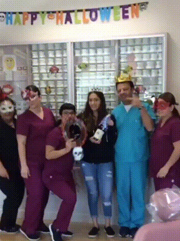 Orthodontic office staff and visitors celebrate Halloween in colorful costumes in front of supply cabinets.