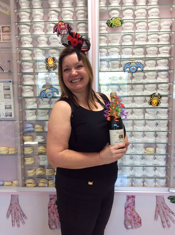 Woman holding flowers smiling in front of orthodontic supplies display wall.