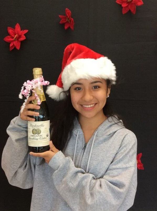 Woman wearing Santa hat holding wine bottle against black background with red decorative elements.