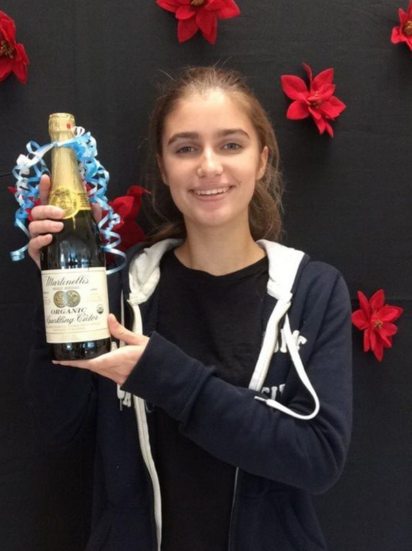 Young girl holding wine bottle award in front of holiday decorations at Brenn Orthodontics